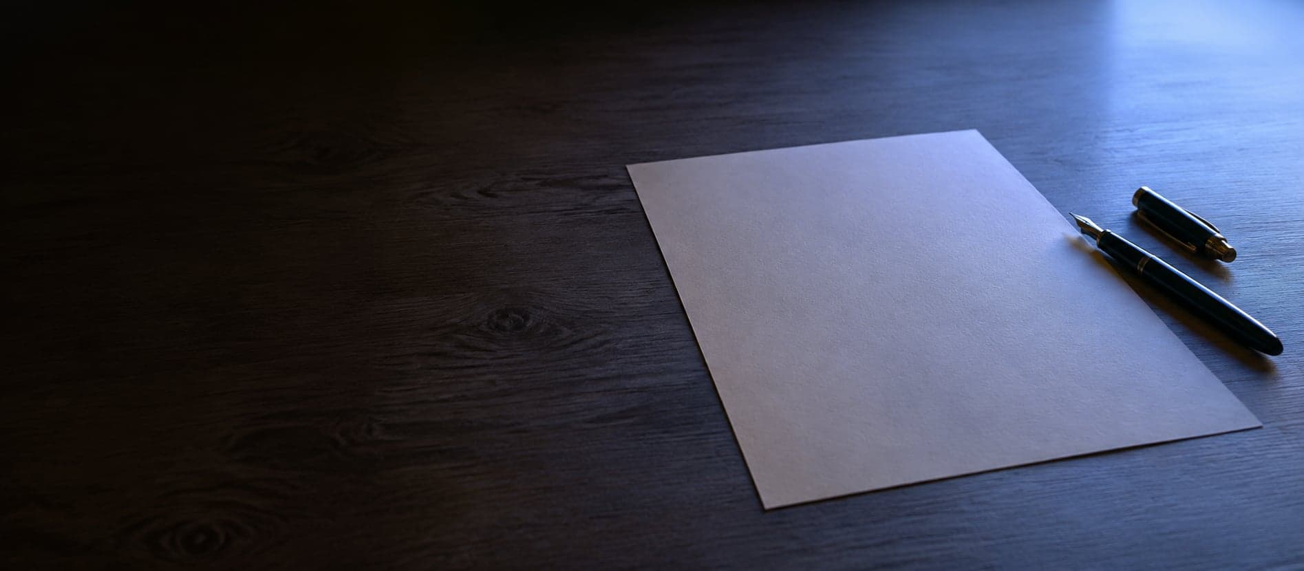 Uma mesa simples na luz baixa da manhã, com uma única folha de papel e uma caneta: o instante antes de começar.